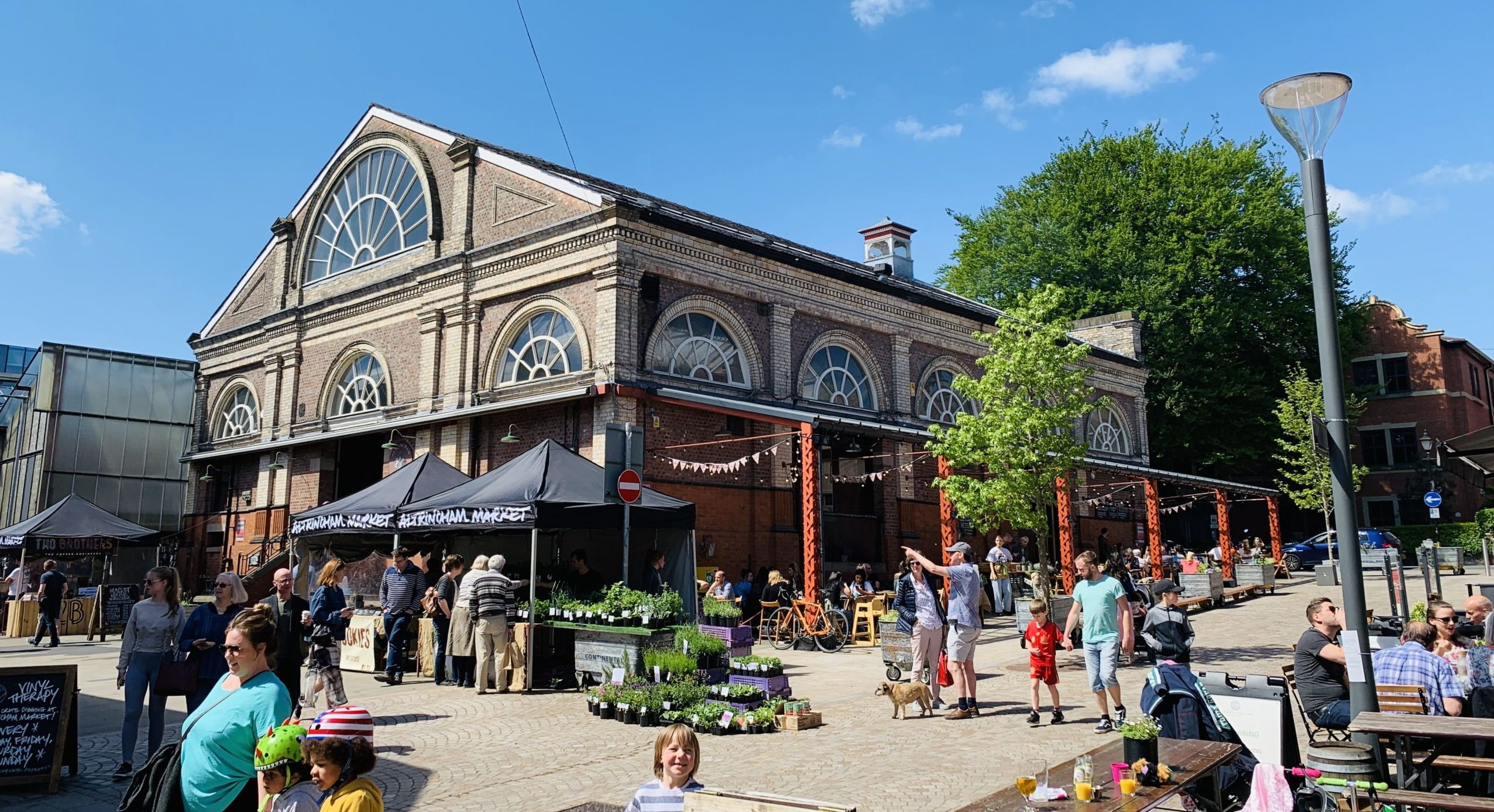Historic market hall surrounded by covered shops and shoppers in the sun.