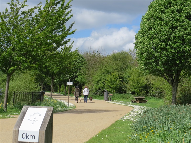 Surfaced footpath lined with trees, with people walking along and a wooden signpost