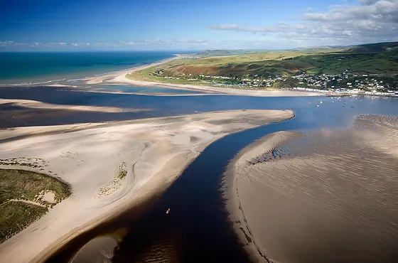 A river estuary flowing into the sea with elevated land in the background.