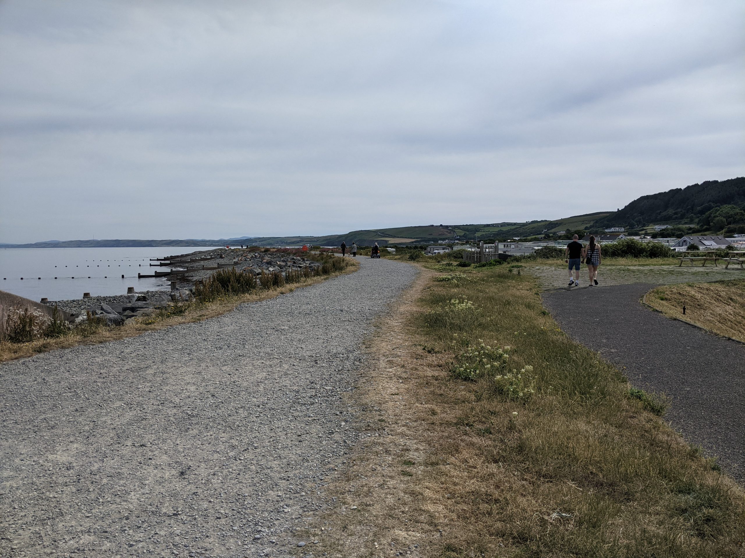 People walking along a seafront gravel path.