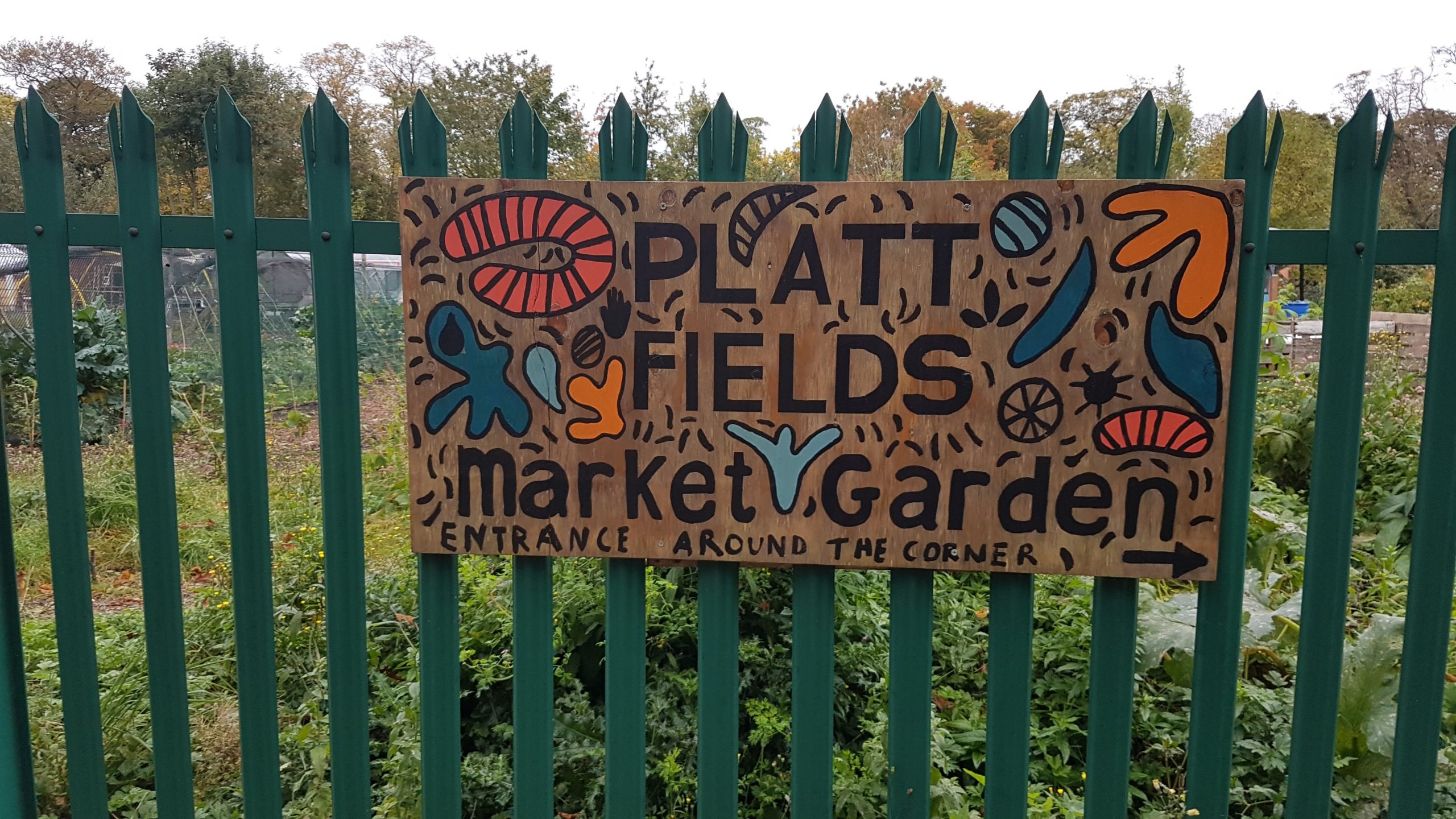 A wooden sign on a fence advertising Platt Fields Market Garden