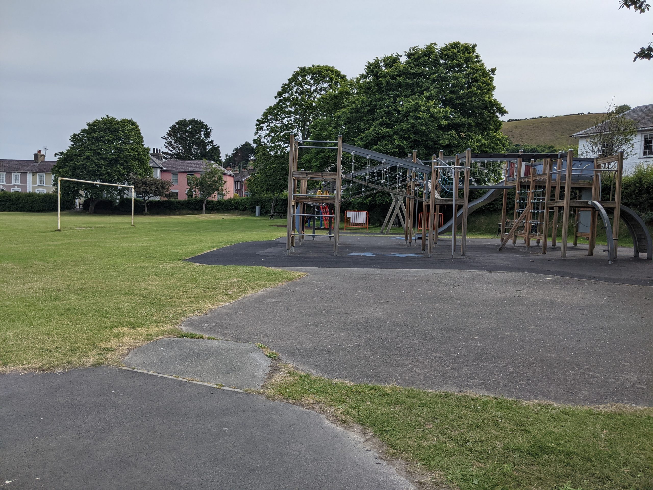 Grass area with housing in the background, football goalposts and a wooden and metal installed play area.