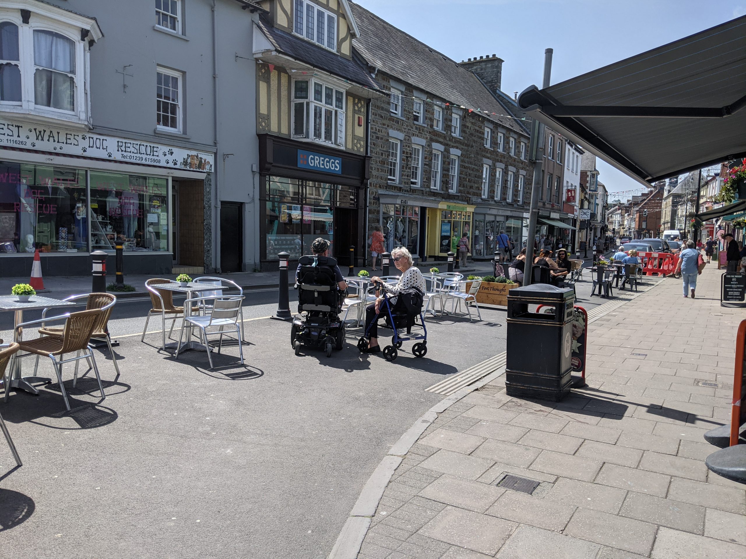 Town centre pedestrianised street with cafe and people sat at outdoor seating.