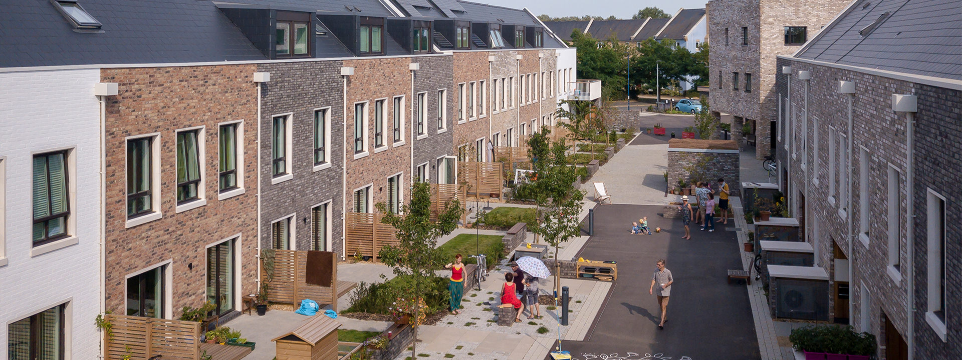 Aerial view of pedestrianised street with new town houses facing onto it, gardens, trees and children playing in the centre.